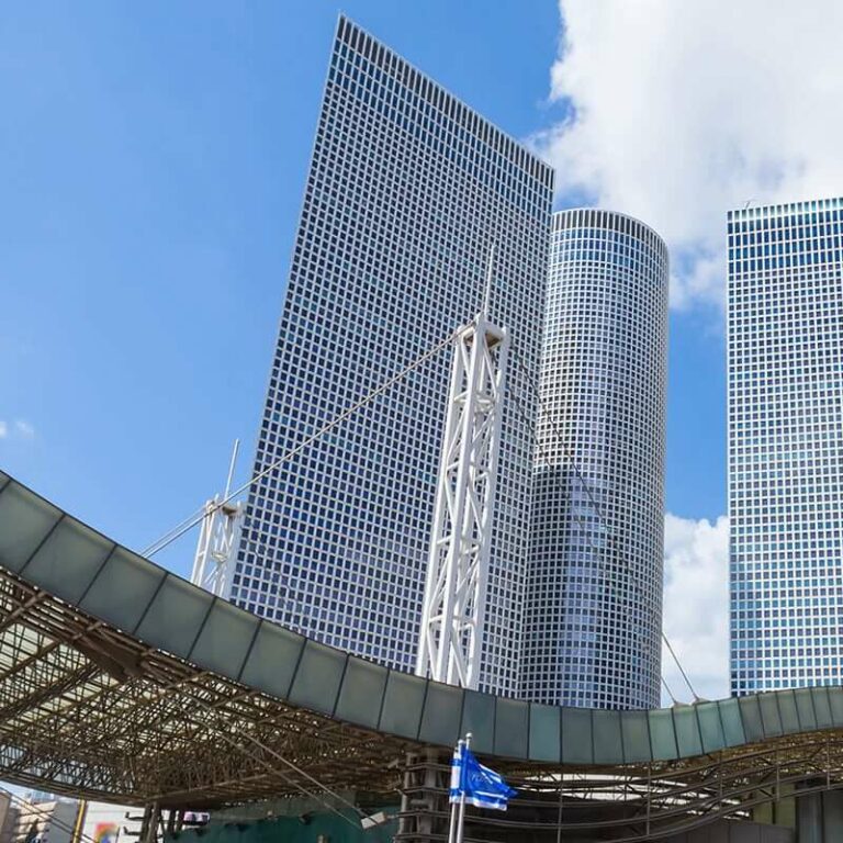 Azrieli towers and mall with flag flying outside under cloudy sky.